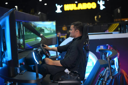 A young man plays a racing simulator game, gripping the steering wheel in a dark room with neon blue lights.
