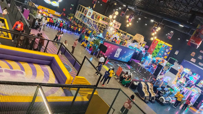 An indoor amusement park with children and adults enjoying various attractions like trampolines and arcade games.