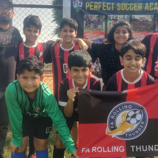 Group of children holding a flag with a logo on a soccer field