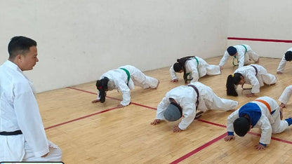 Group of people practicing martial arts on a wooden floor with a white wall background
