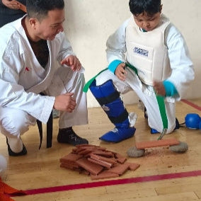 Two martial arts practitioners preparing for a training session with belts and equipment on a wooden floor.