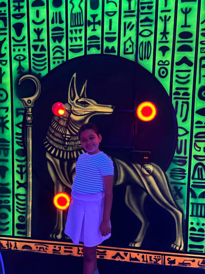 Child standing in front of a glowing Anubis statue with hieroglyphics on a dark background