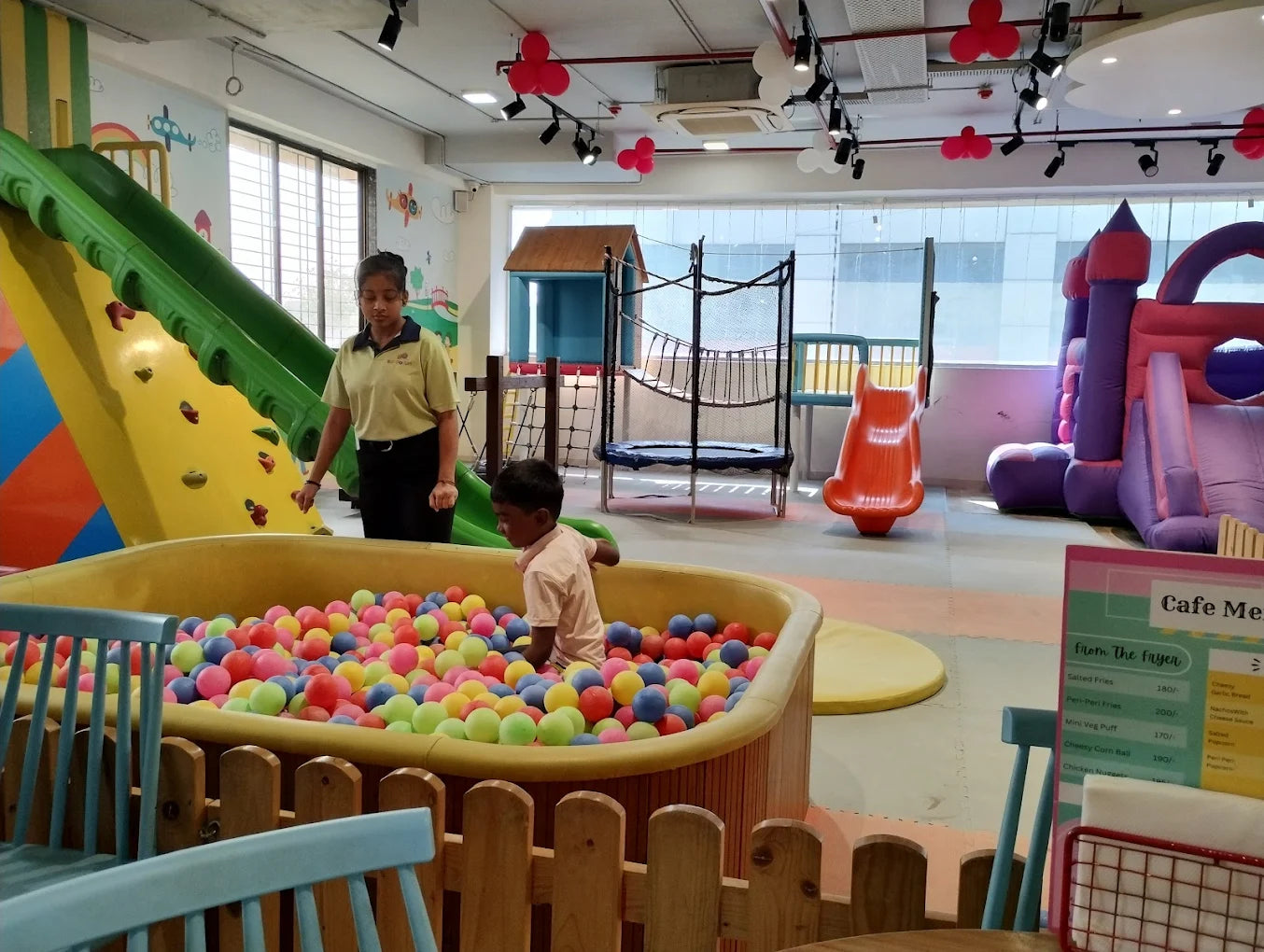 Children play in a ball pit at an indoor playground with slides and a bouncy castle.