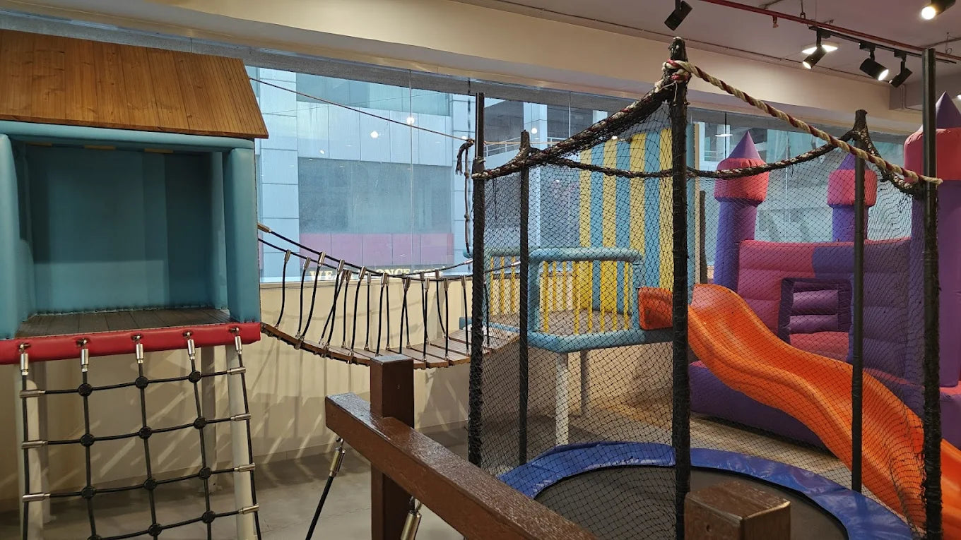 An indoor playground with a bouncy castle, slide, rope bridge, and climbing net for children.