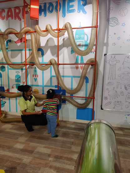 A woman helps a young child play with a tube system in a colorful, space-themed room.