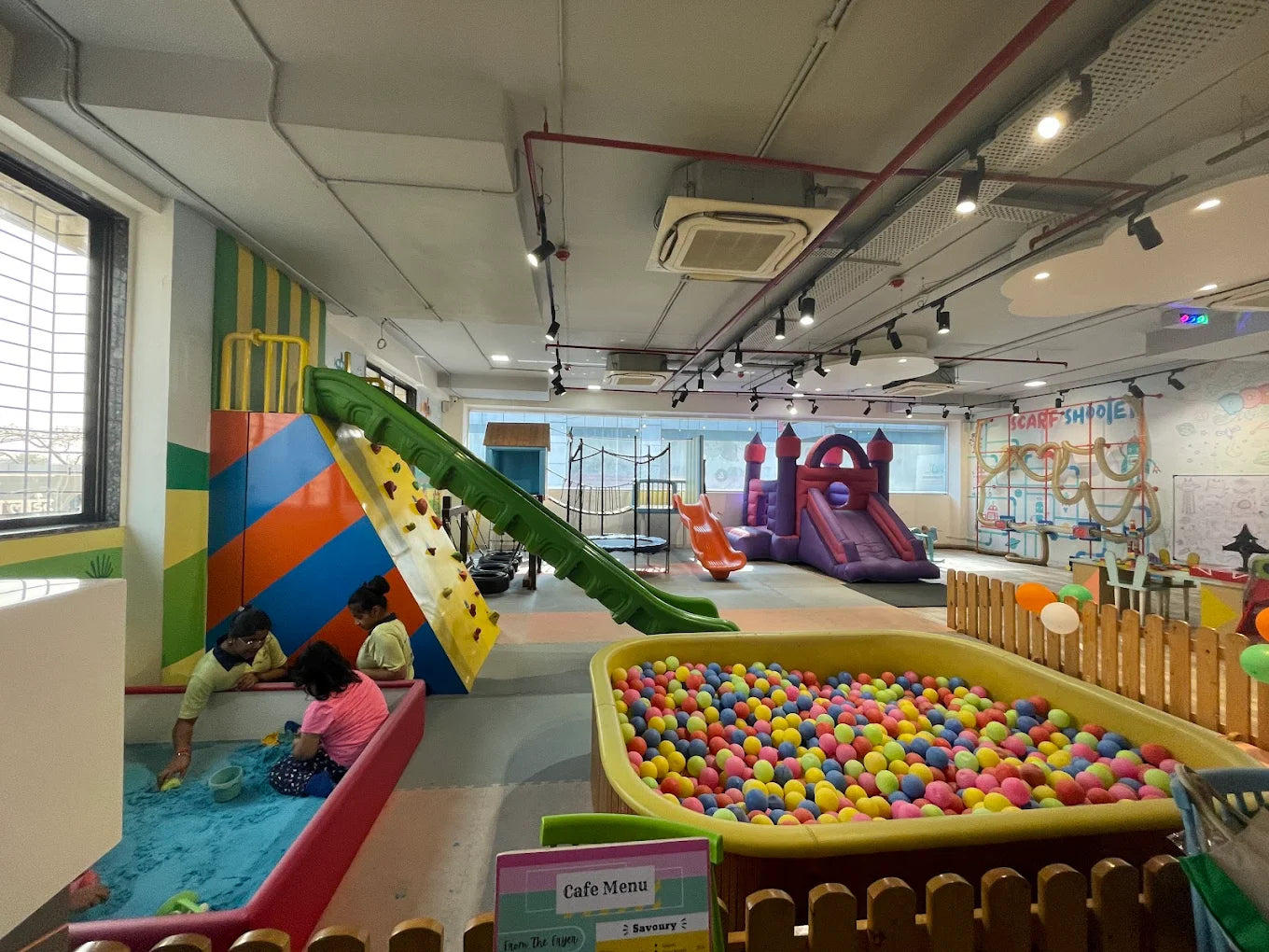 Children play in a colorful indoor playground with a ball pit, slides, and a climbing wall.