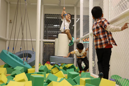 Children play in a soft play area with foam blocks and swings.