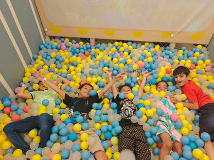 Children lie in a ball pit, smiling and playing.