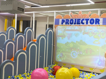 A ball pit with a projected game for children, featuring colorful balls and soft play structures.