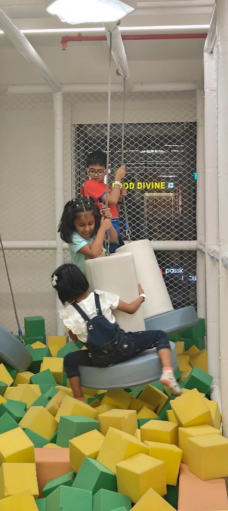 Children play in a foam pit with large soft blocks and a swing.