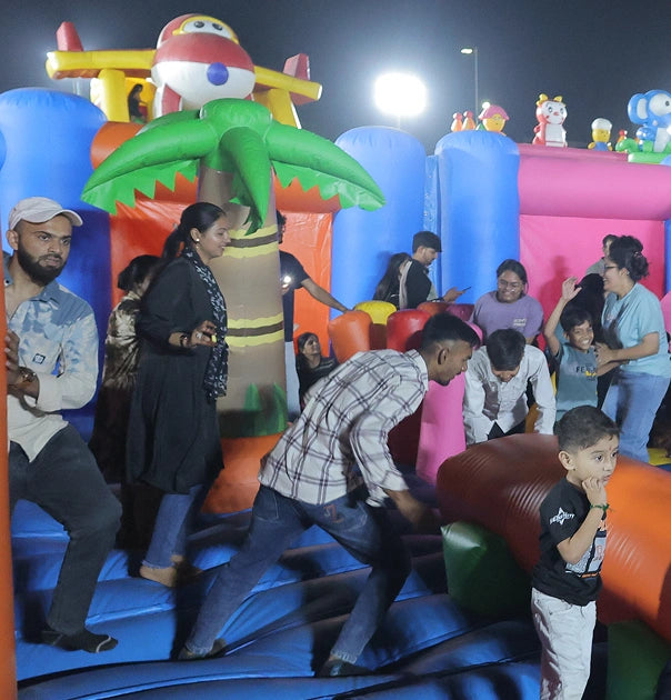 Children and adults enjoy an inflatable playground with a plane and palm tree theme at night.