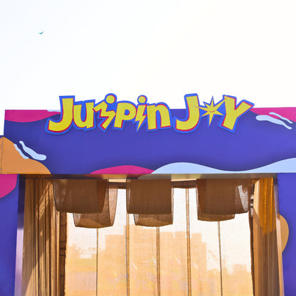 A colorful sign reads "Juspin Joy" above a stage with burlap and sheer curtains.