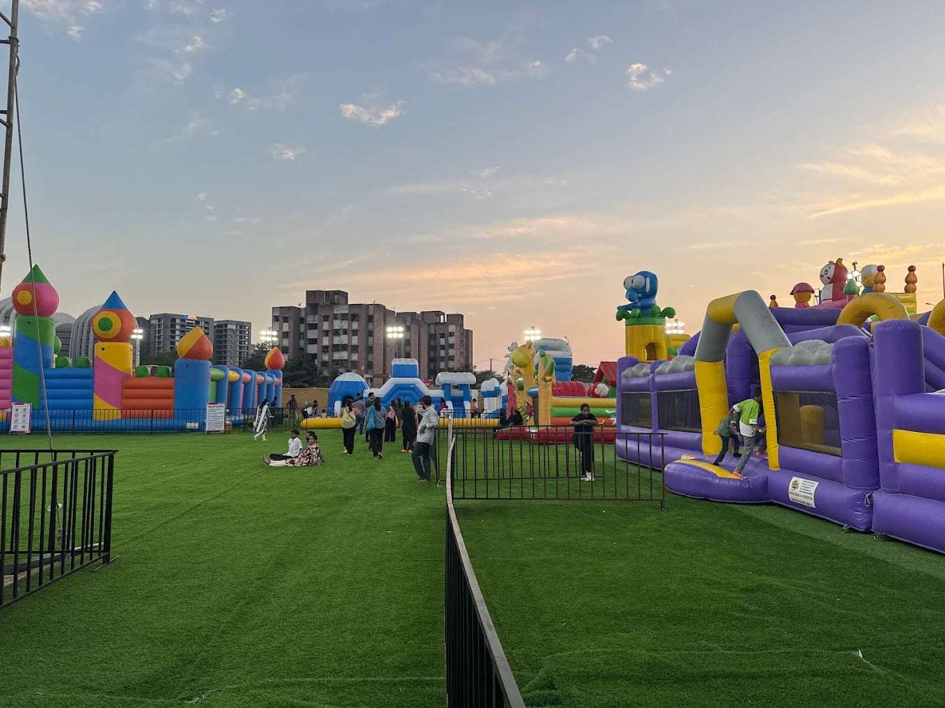 Children play on a large inflatable playground with colorful castles and obstacles under a sunset sky.