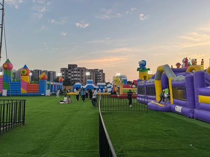 Children play on a large inflatable playground with colorful castles and obstacles under a sunset sky.