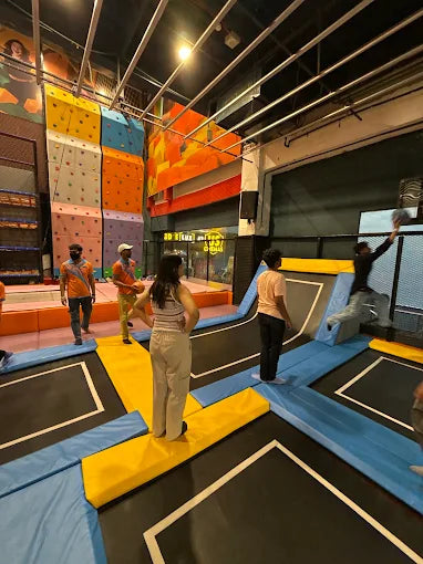 People jump on trampolines in an indoor adventure park with climbing walls.