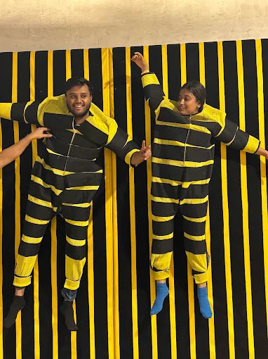 Two young people in bee costumes lie on a black and yellow striped background.