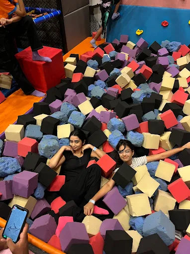 Two young women relax in a foam pit at a trampoline park.