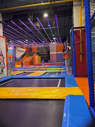 An indoor trampoline park with colorful padded areas and a person standing.