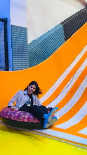A young woman laughs as she slides down an orange and white striped slide on an inflatable tube.