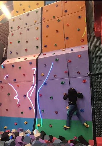 A child climbs a colorful indoor rock wall with glowing lines.