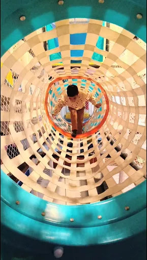 A child crawls through a netted tunnel at a playground.