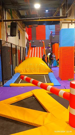 An indoor trampoline park with colorful obstacles and people enjoying the activities.
