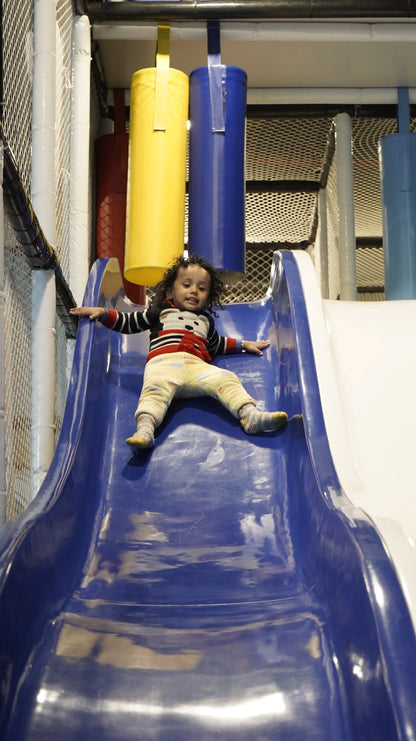 A young child slides down a blue playground slide.