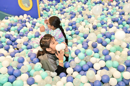 Two young girls play in a ball pit filled with blue, white, and teal balls.