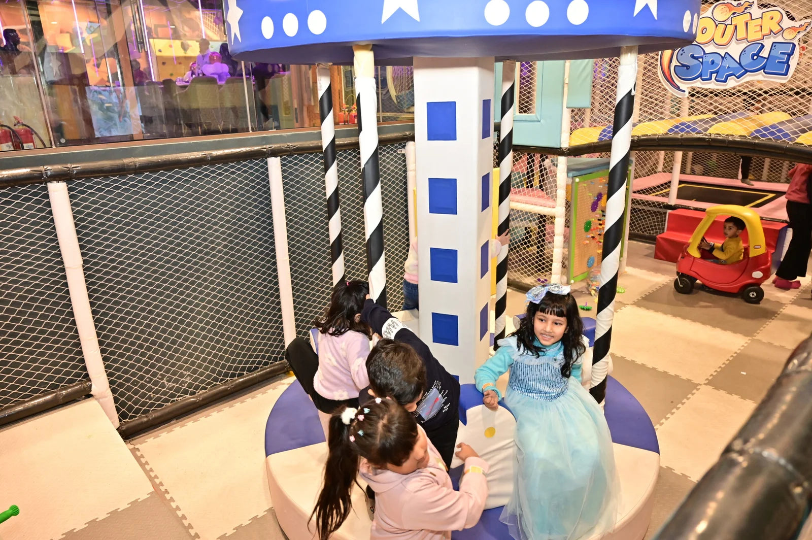 Children play in a colorful indoor playground with a carousel and a toy car.