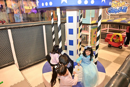 Children play in a colorful indoor playground with a carousel and a toy car.