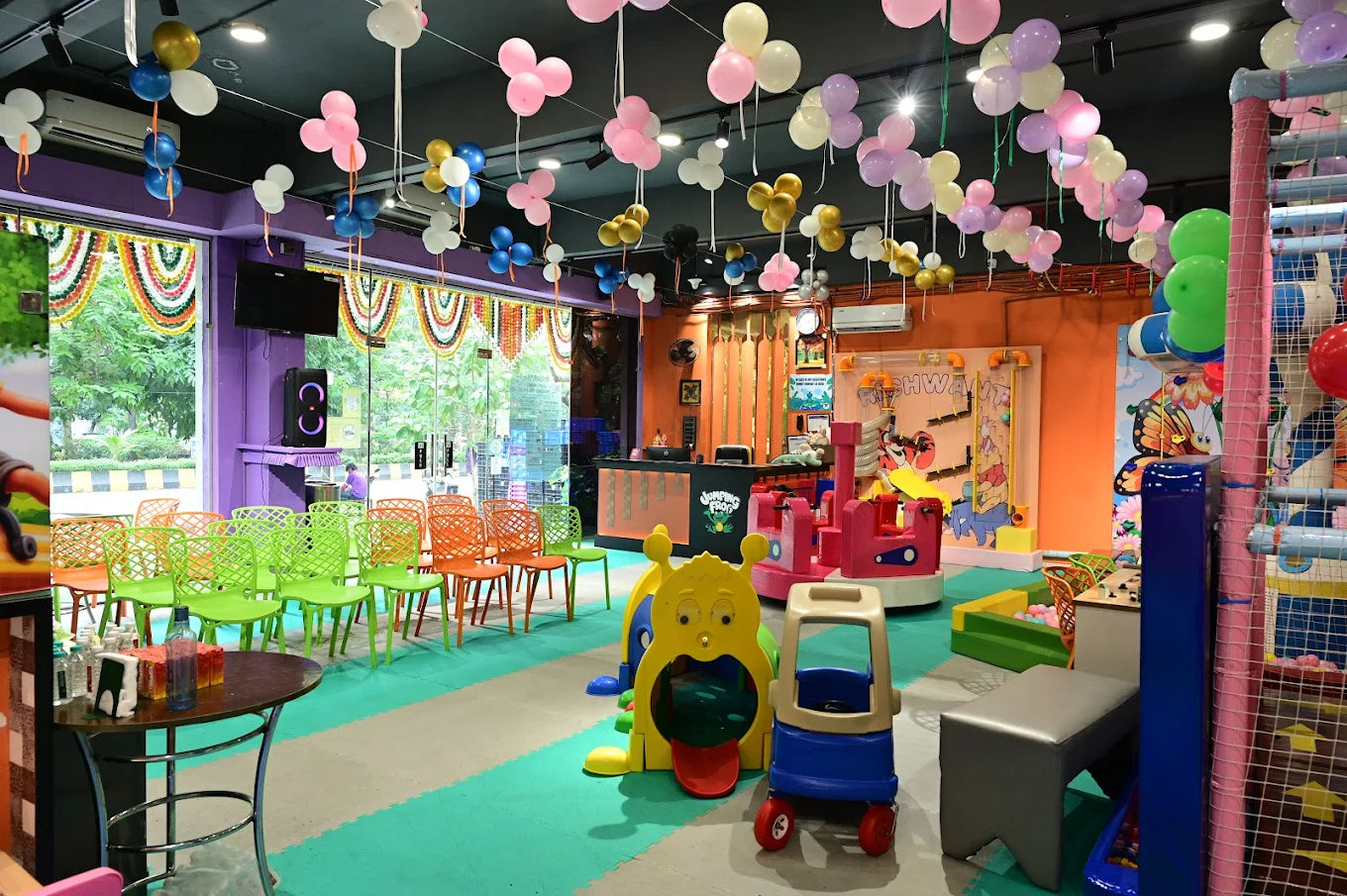 A colorful indoor playground with balloons, toys, and seating for children.