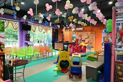A colorful indoor playground with balloons, toys, and seating for children.