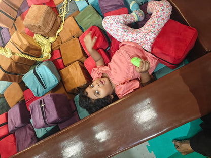 A young child lies on a pile of colorful soft blocks, holding a green toy.