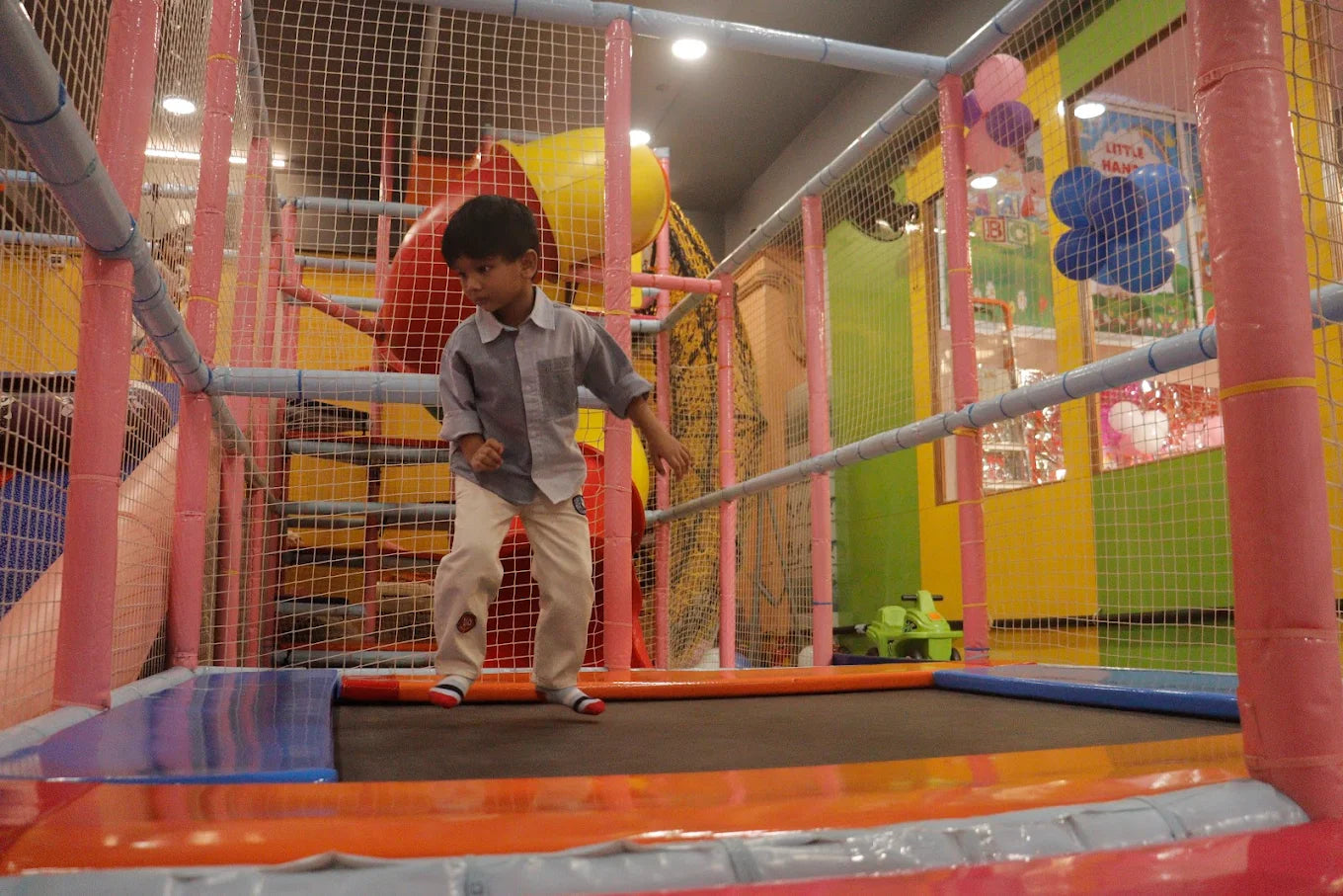 A young boy jumps on a trampoline in a colorful indoor playground.
