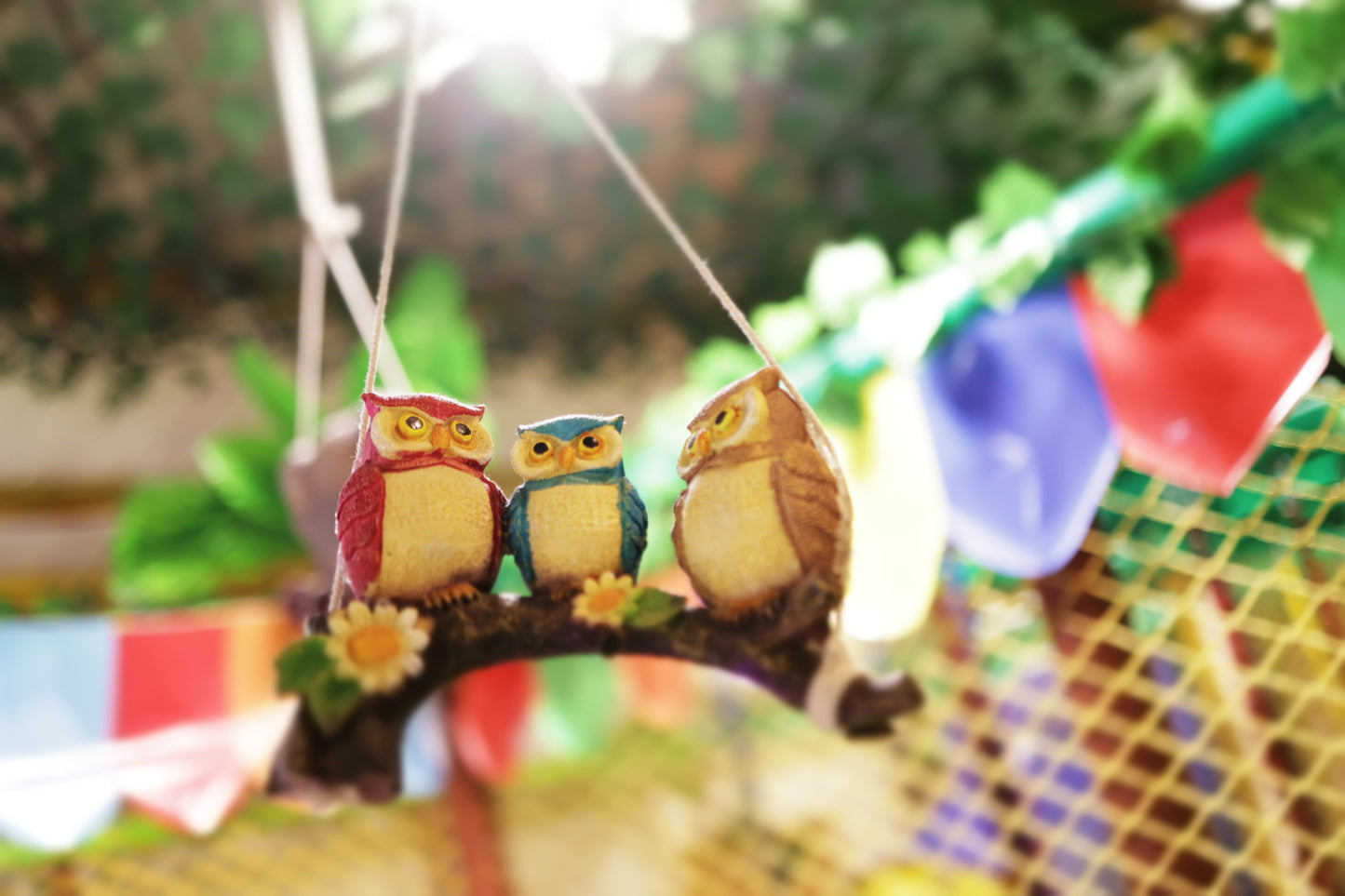 Three decorative owls perched on a branch hanging inside a vibrant play area with colorful flags in the background