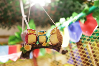 Three decorative owls perched on a branch hanging inside a vibrant play area with colorful flags in the background
