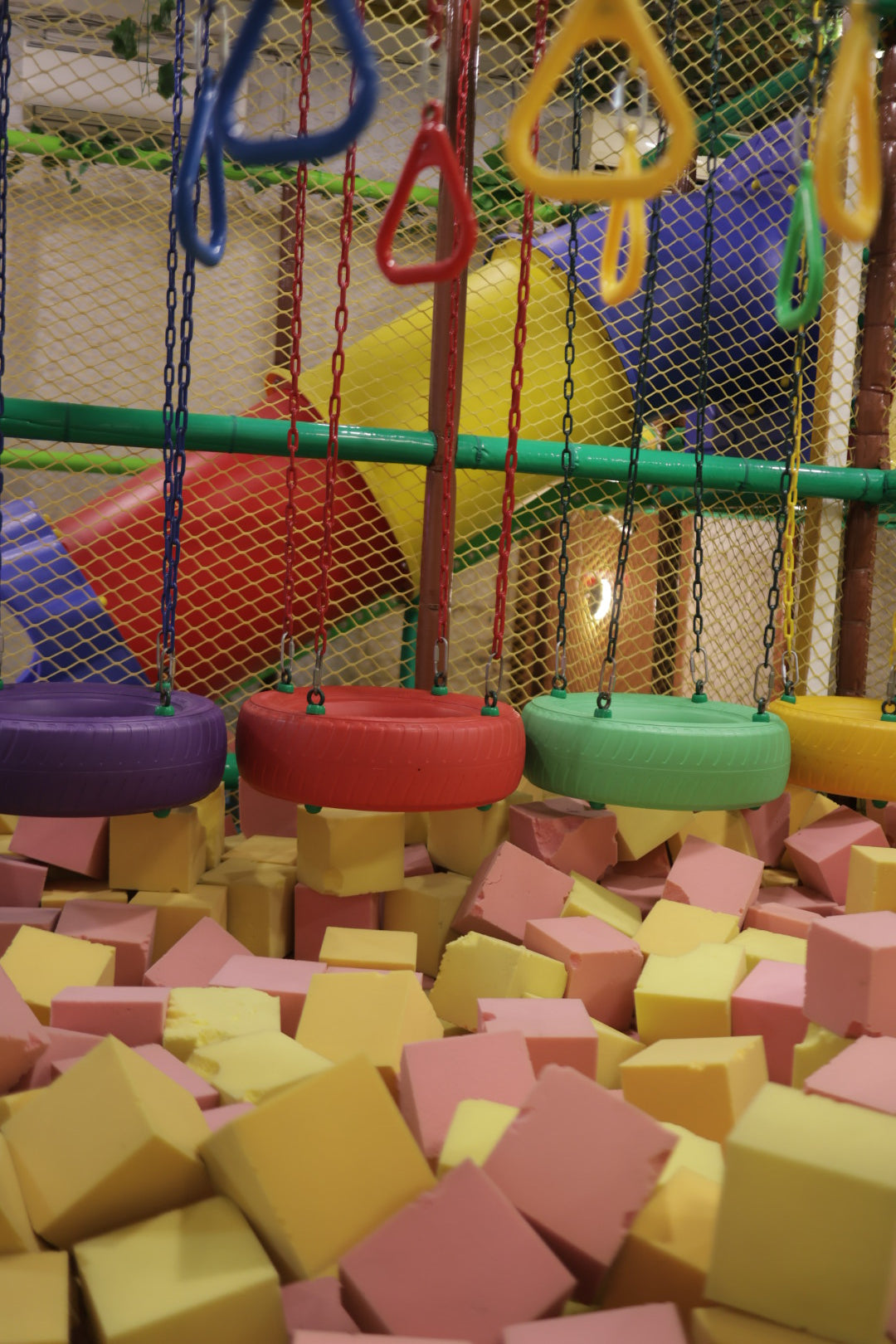 Colorful hanging tire swings above soft foam blocks in vibrant indoor play area at Jumping Jollies Sector 104 Hazipur