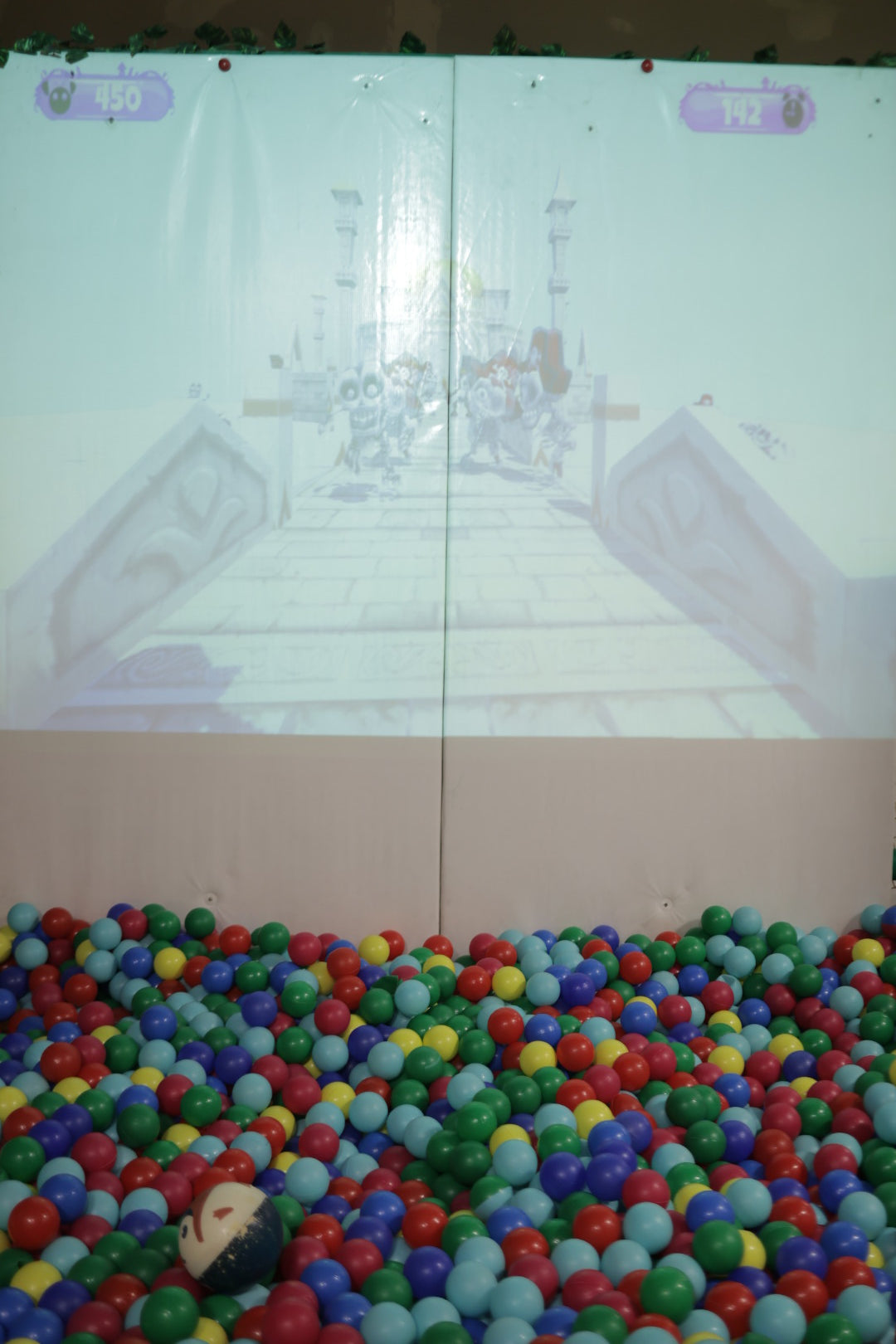 Projection of an adventure game displayed above a colorful ball pit filled with red, blue, green, and yellow balls at indoor play area