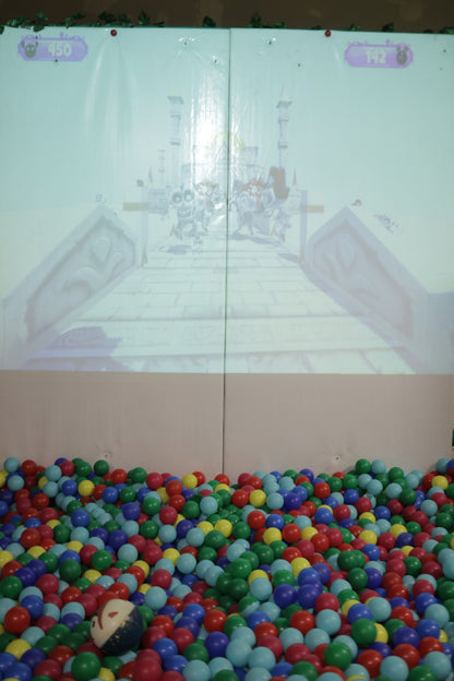 Projection of an adventure game displayed above a colorful ball pit filled with red, blue, green, and yellow balls at indoor play area