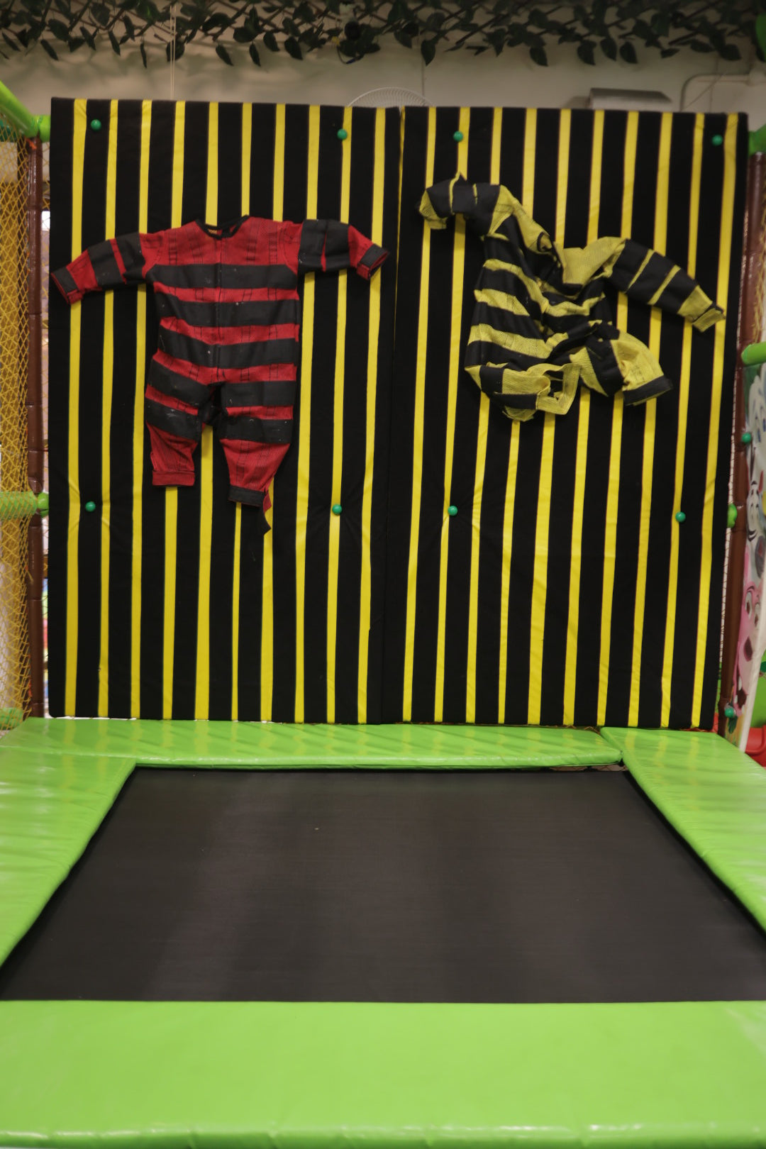 Interactive vertical wall with sticky suits in red and yellow stripes above lime green trampoline at Jumping Jollies Sector 104 Hazipur