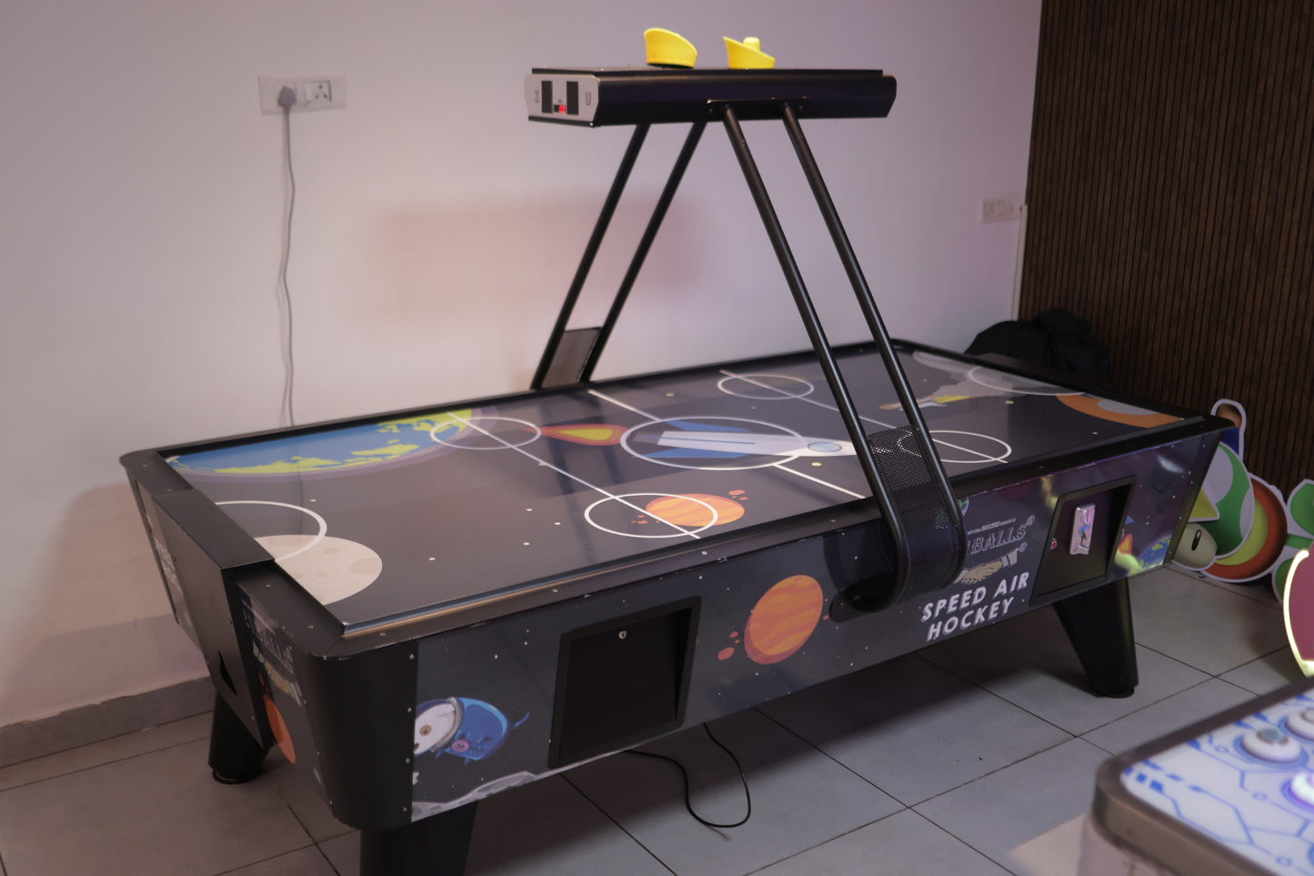 Space-themed air hockey table with controls on a tiled floor.