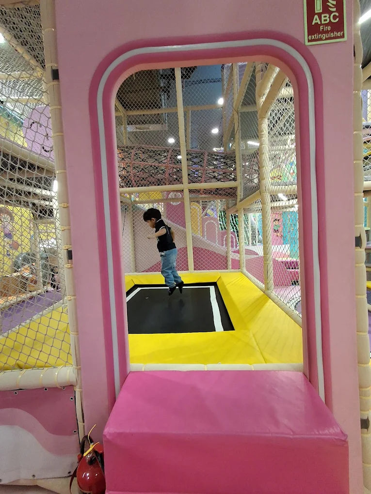 A child jumps on a trampoline in a colorful indoor playground.