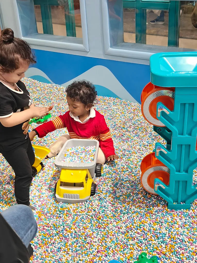 Two young children play with toys in a ball pit filled with colorful balls.