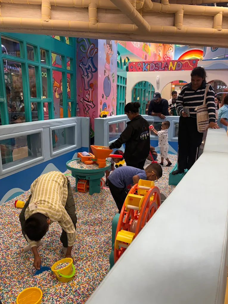 Children play in a ball pit at an indoor playground with colorful walls and structures.
