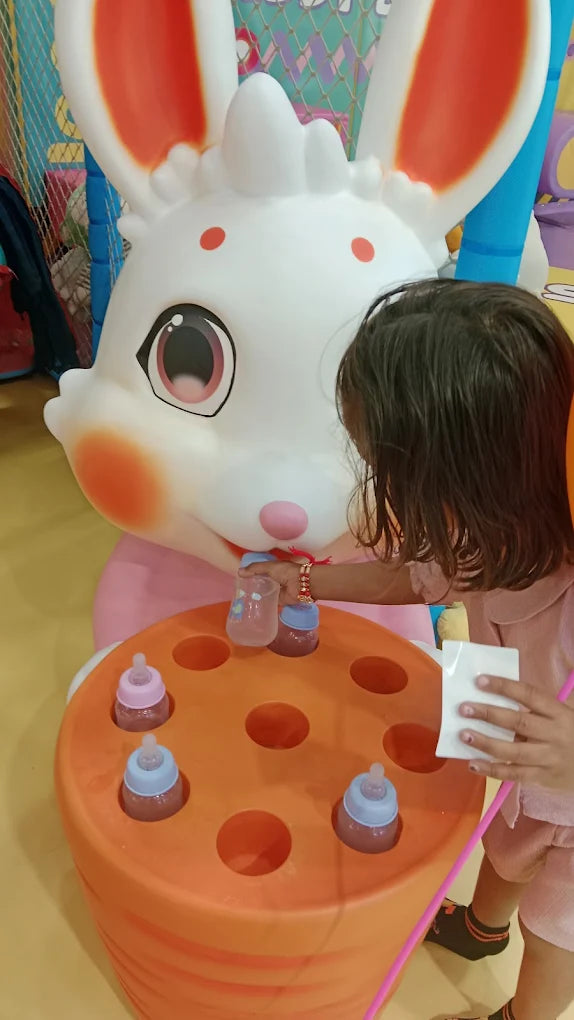 A young child plays with baby bottles in a colorful play area, interacting with a large bunny decoration.