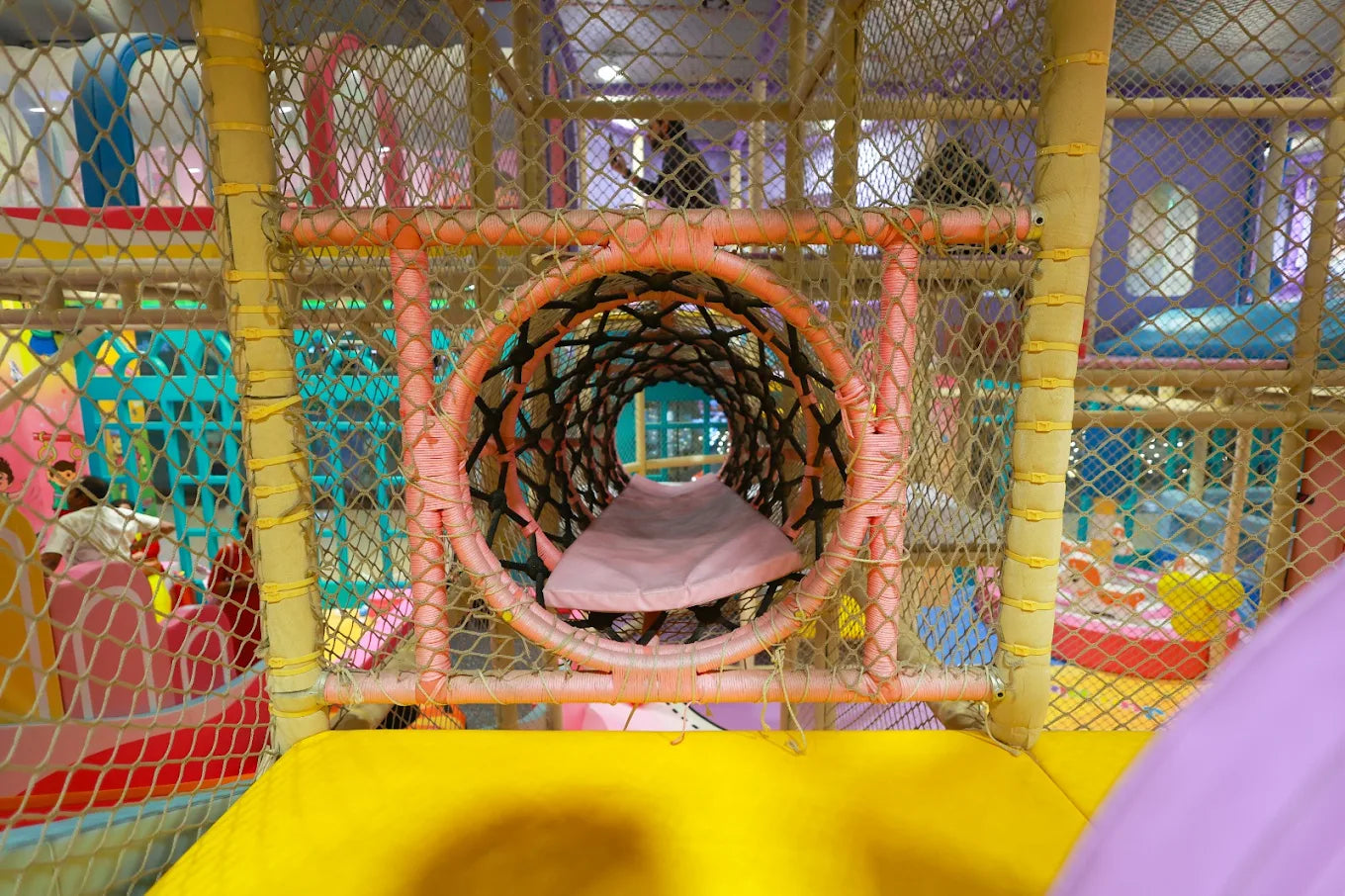 A colorful indoor playground with a net tunnel and children playing.