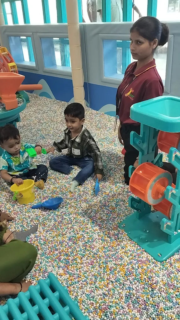 Children play in a ball pit with a woman supervising.
