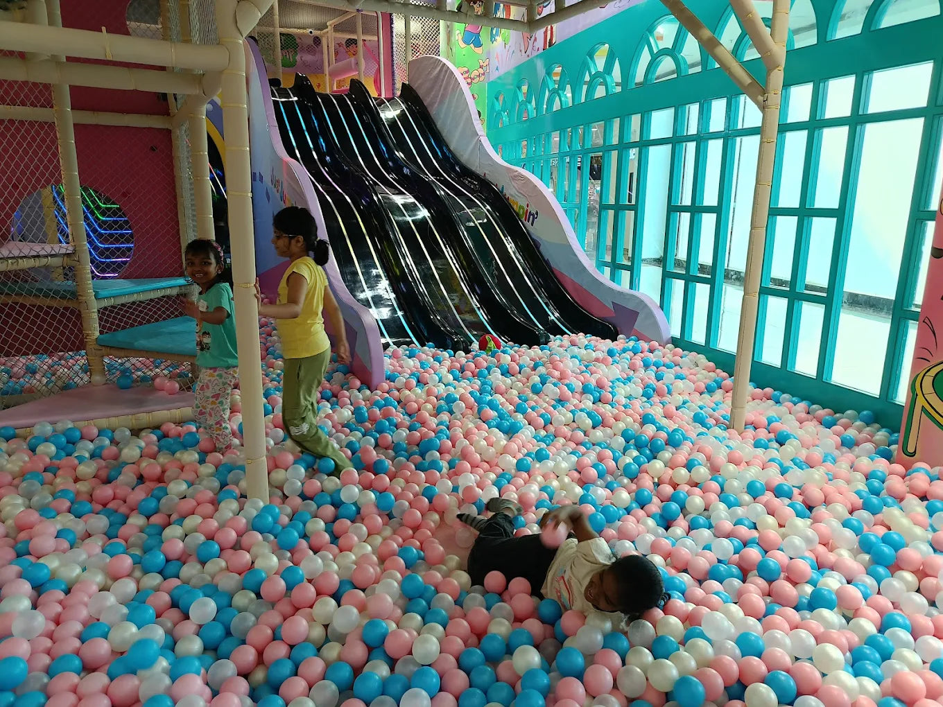 Children play in a ball pit with slides in an indoor playground.
