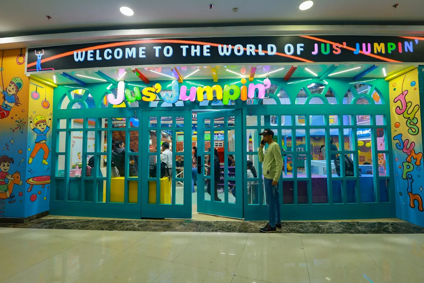 A brightly colored entrance to a children's play area called "Jus' Jumpin'" with a man on his phone outside.