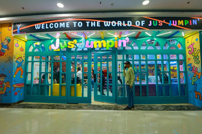 A brightly colored entrance to a children's play area called "Jus' Jumpin'" with a man on his phone outside.